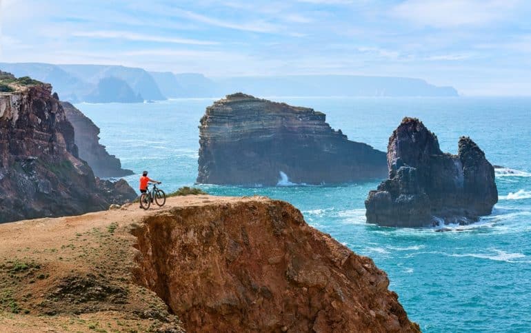happy active senior woman cycling on the the rocky cliffs of the Vicentina coast of Portugal near Sagres and Vila do Bispo "cliffs,alentejo landscape,bicycle,happy,scenic,one person,fitness,weather,season,alentejo,female,rota vicentina,sky,coastline,active,electric bicycle,girl,vicentina,water,adventure,coast,sand,atlantic,panorama,ocean,aljezur,senior woman,mountain biking,cliff,portugal,scenery,rocky,sea,summer,wave,rock,seascape,electric bike,mountain bike,vacation,algarve,cyclist,nature,shore,outdoor,outdoors,beach,travel,sport,landscape"